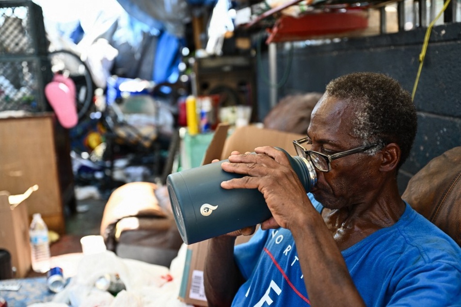 Warren Smith, a US Army veteran, drinks water while sitting under shade with friends in "The Zone."