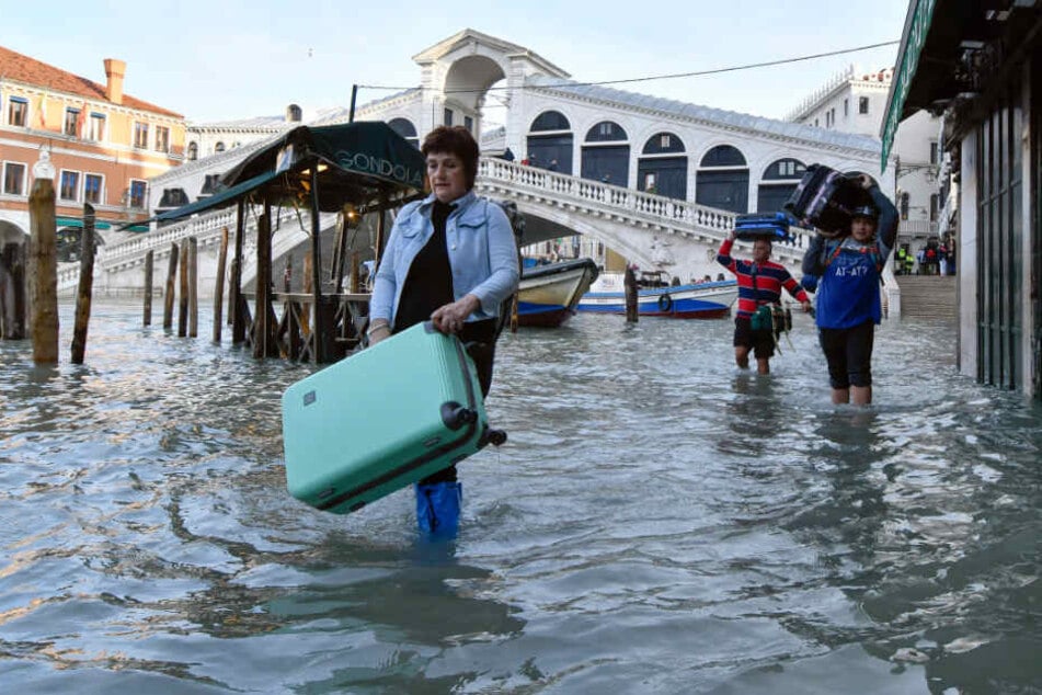 Touristen tragen ihr Gepäck bei einem Hochwasser mit einem Pegel von 1,44 Metern in der Nähe der Rialtobrücke durch eine Straße.