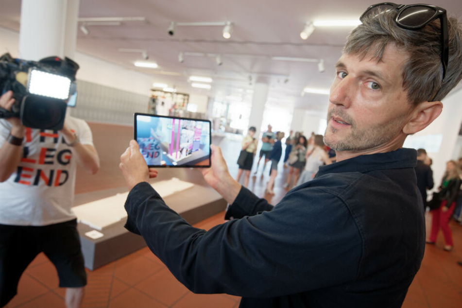 Der Künstler Ulf Aminde hält ein Tablet, auf dem die virtuellen Wände des geplanten Mahnmals für die Opfer der NSU in Köln zu sehen sind.
