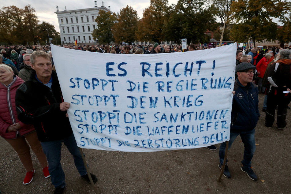 Teilnehmer einer Demonstration gegen die Energiepolitik versammeln sich vor dem Schweriner Schloss. Auf einem Transparent steht "Es reicht! Stoppt die Regierung Stoppt den Krieg Stoppt die Sanktionen Stoppt die Waffenliefer. Stoppt die Zerstörung Deu's".