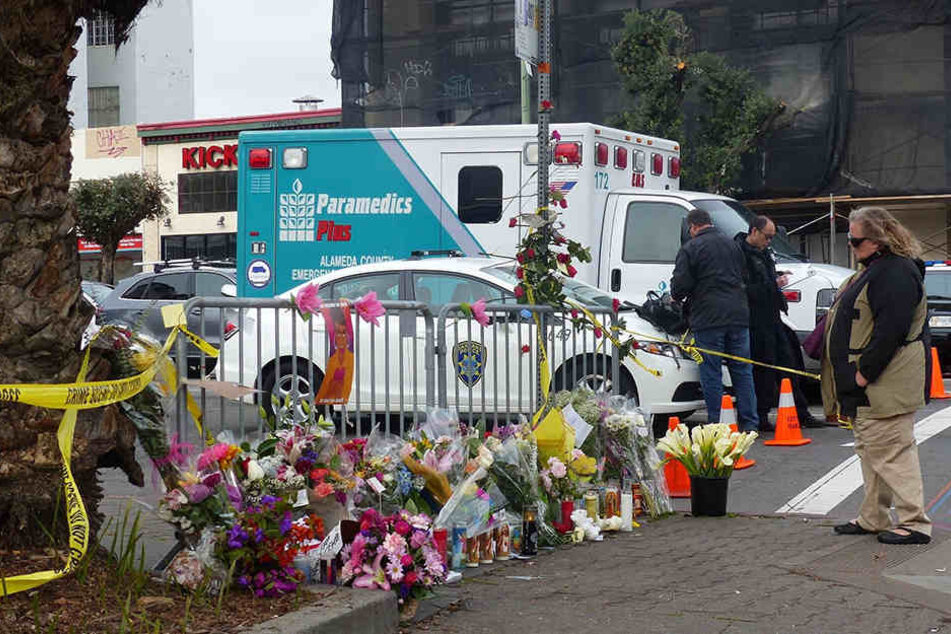 Hunderte Blumen und Andenken liegen auf dem Gehweg vor der ausgebrannten Lagerhalle.
