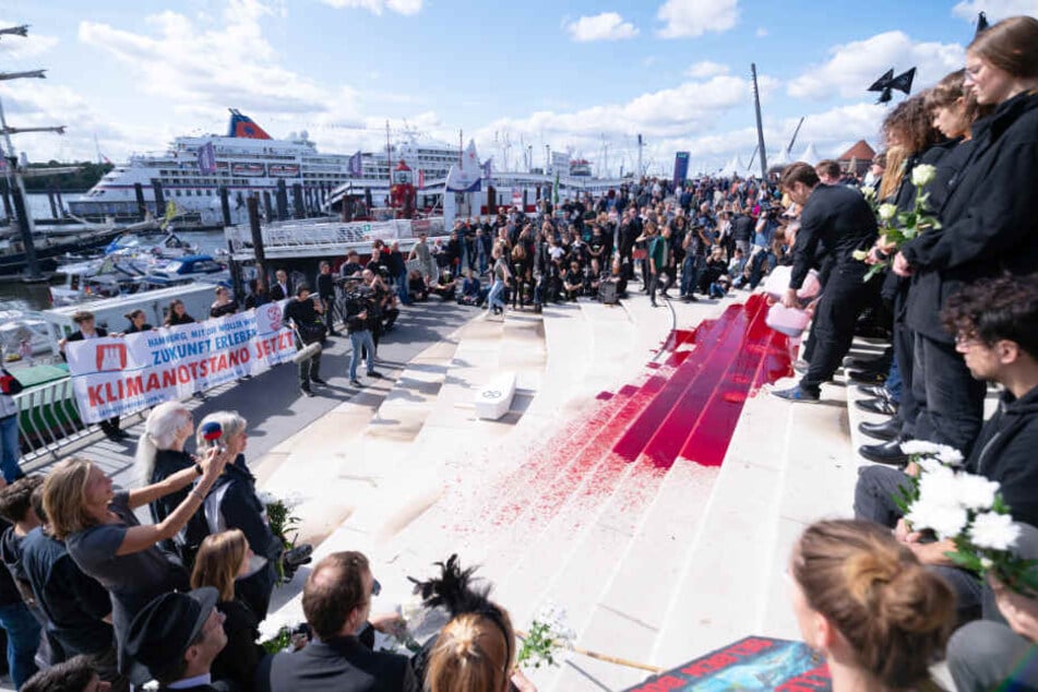 Aktivisten der Gruppierung Extinction Rebellion schütten während der Hamburg Cruise Days eine blutrote Flüssigkeit auf Treppen am Hafen.