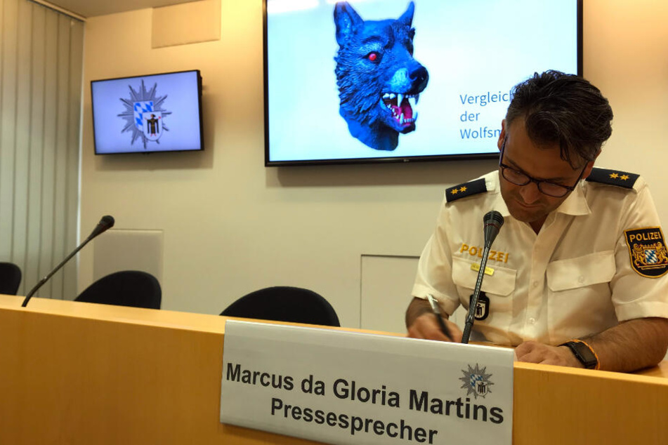 Marcus da Gloria Martins, Sprecher der Münchner Polizei, bei einer Pressekonferenz. Im Hintergrund ist ein Vergleichsbild der Wolfsmaske zu sehen.