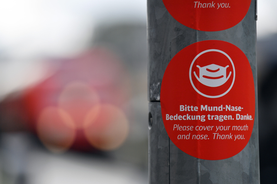 "Bitte Mund-Nase-Bedeckung tragen" steht in deutscher und englischer Sprache auf einem Aufkleber (Symbolbild).