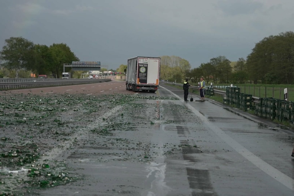 Zerstörte Bierflaschen liegen auf der Autobahn, während an der Straßenseite Bierkästen stehen.