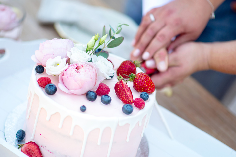 Ein Brautpaar schneidet eine Torte bei der Hochzeitsfeier an.