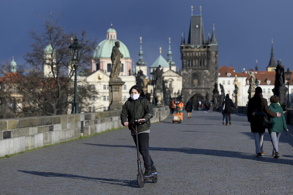Ein Junge mit Schutzmaske fährt einen Roller auf der Karlsbrücke in Prag.