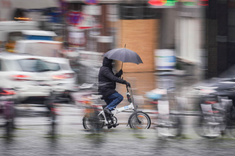 Ein Radler schützt sich während der Fahrt durch Frankfurt mit einem Schirm vor der Nässe.
