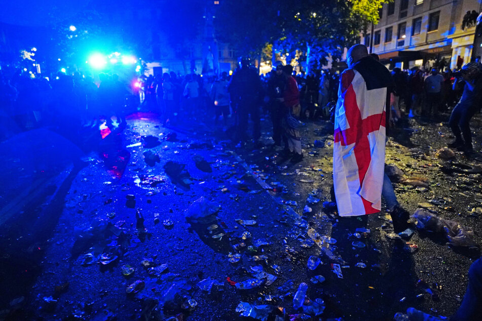 Ein englischer Fan, der in eine Flagge gehüllt ist, geht durch Müll und zerbrochenes Glas auf dem Trafalgar Square.