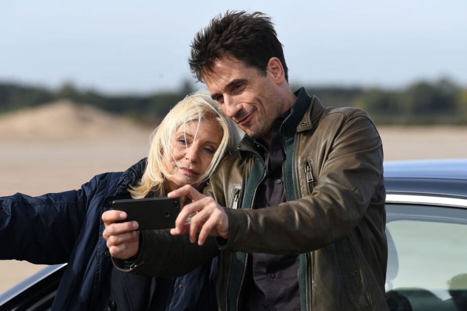 Schauspieler Oliver Mommsen macht mit Schauspielerin Sabine Postel am Rande der Dreharbeiten ein Selfie.