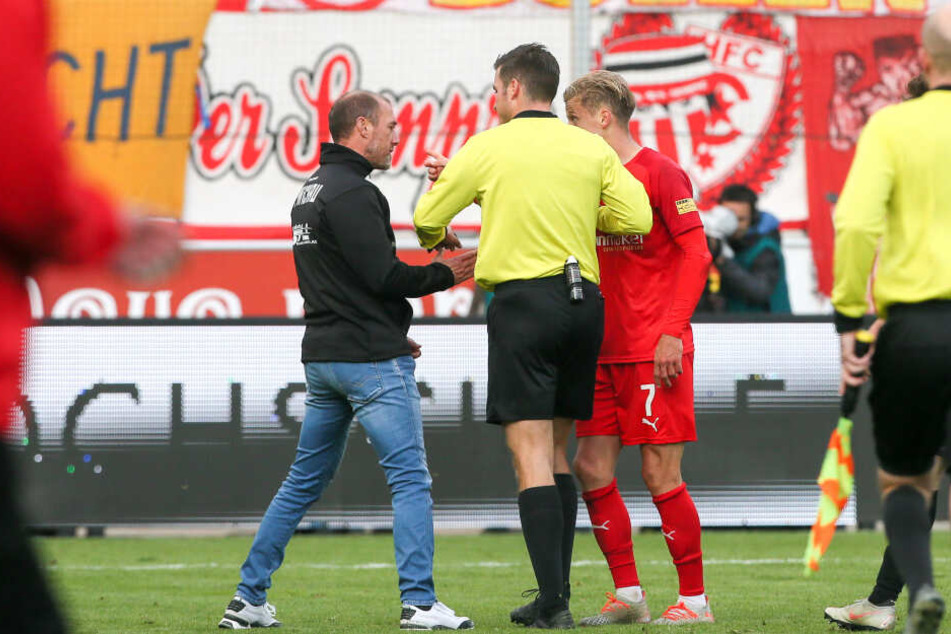 Schiedsrichter Harm Osmers (m.) trennt Trainer Joe Enochs (l.) und Bentley Bexter Bahn.