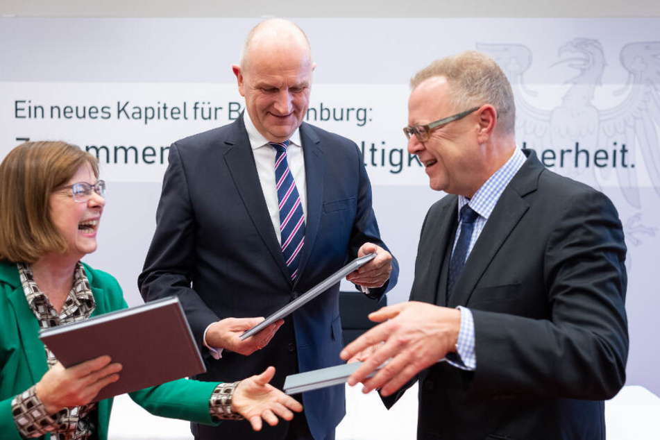 Dietmar Woidke (M), Michael Stübgen (r) und Ursula Nonnemacher tauschen die Mappen mit dem unterschriebenen Koalitionsvertrag aus.