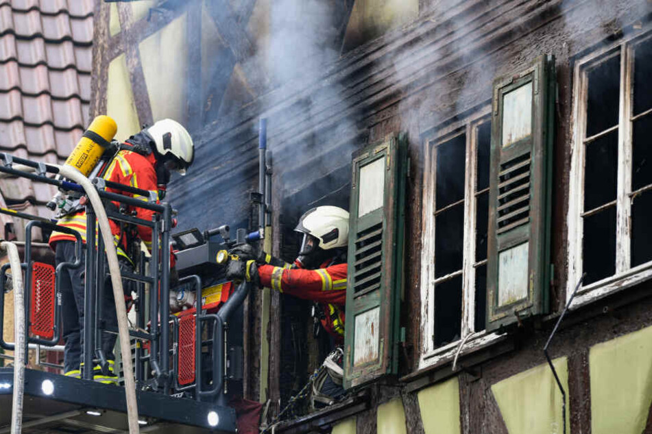 Ein Feuerwehrmann kommt aus einem Fenster in dem brennenden Haus und wird von seinem Kollegen an der Drehleiter gesichert.