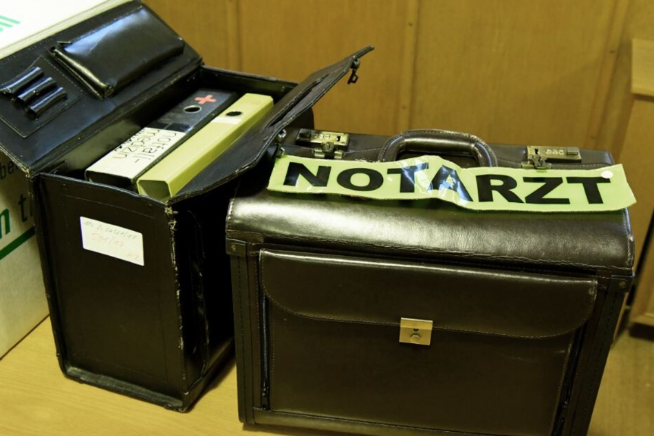 Ein Koffer mit Notarzt-Abzeichen und weitere Beweismittel stehen beim Prozessauftakt im Gerichtssaal.