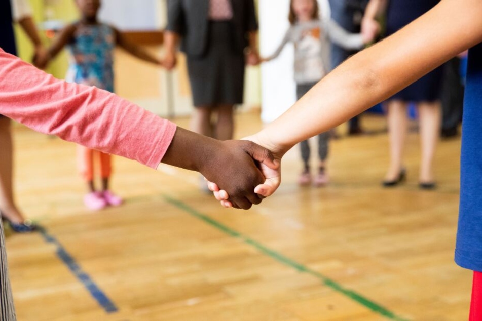 Hand in Hand tanzen Kinder und Erzieherinnen bei einem Bewegungsspiel in der Turnhalle einer Kita