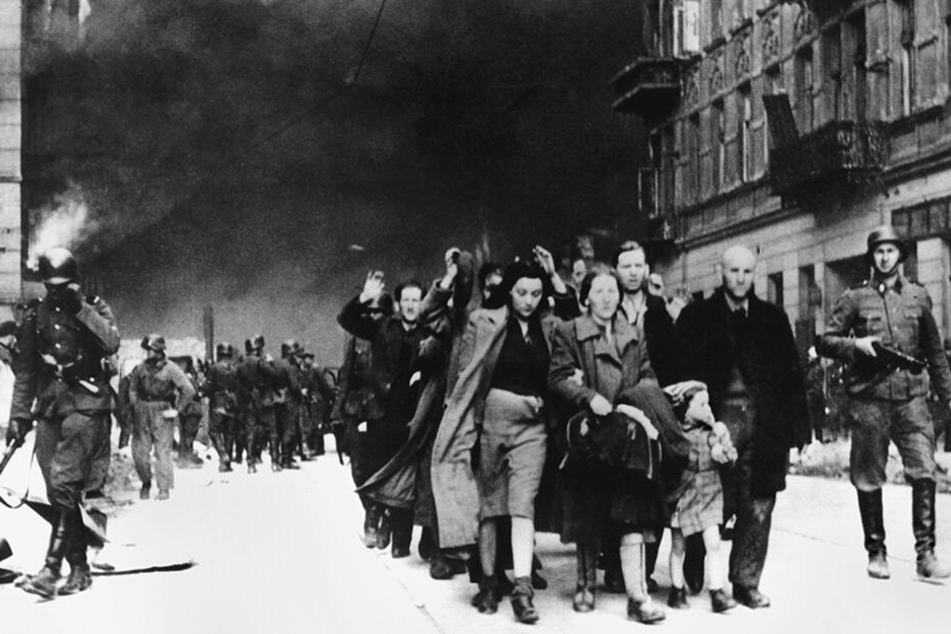 Warschau, Mai 1943: Mit erhobenen Händen werden jüdische Frauen, Männer und Kinder von deutschen SS-Soldaten aus dem brennenden Ghetto der polnischen Hauptstadt getrieben.