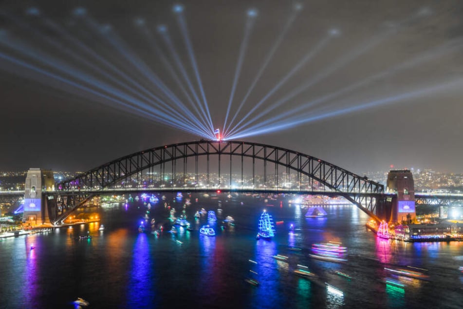 Diese Langzeitaufnahme zeigt Schiffe, die am Ende der Silvesterfeierlichkeiten unter der festlich beleuchteten Harbour Bridge durchfahren.