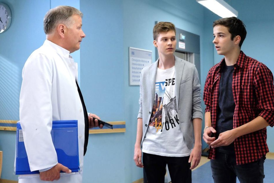 Bastian (M., der Sohn von Sachsenklinik-Verwaltungschefin Sarah Marquardt) und Jonas (r., Dr. Heilmanns Enkel) wollen vom Klinikleiter wissen, wie schnell ihr Sänger Jimmy wieder auf der Bühne stehen und ob der Auftritt stattfinden kann.