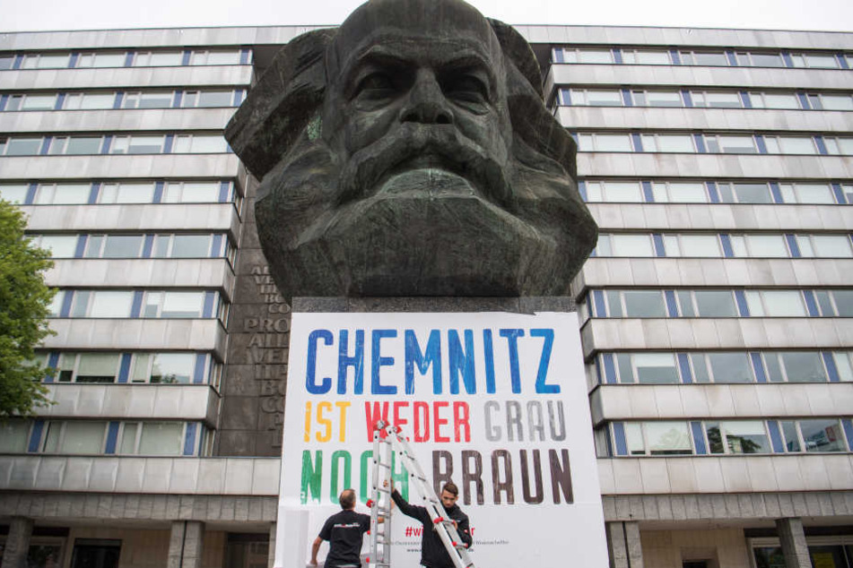 Zwei Männer befestigen am Karl-Marx-Denkmal ein Plakat mit der Aufschrift "Chemnitz ist weder grau noch braun".