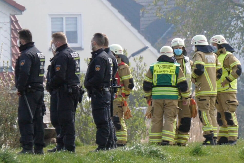 Einsatzkräfte von Polizei und Feuerwehr stehen vor dem Wohnhaus.