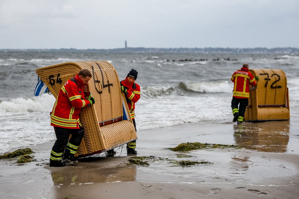 Einsatzkräfte versuchen Strandkörbe am Ostseestrand vor der Sturmflut zu sichern.