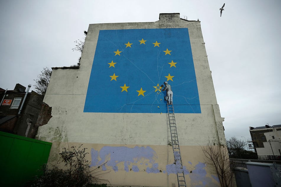 Ein Wandgemälde des Künstlers Banksy zeigt eine EU-Flagge mit einem Handwerker, der einen der Sterne abschlägt.