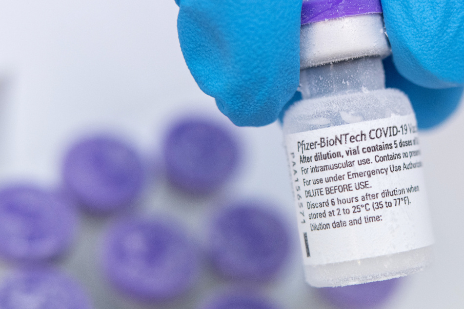Ein Arzt hält eine Ampulle des Corona-Impfstoffs von Biontech und Pfizer zwischen den Fingern.