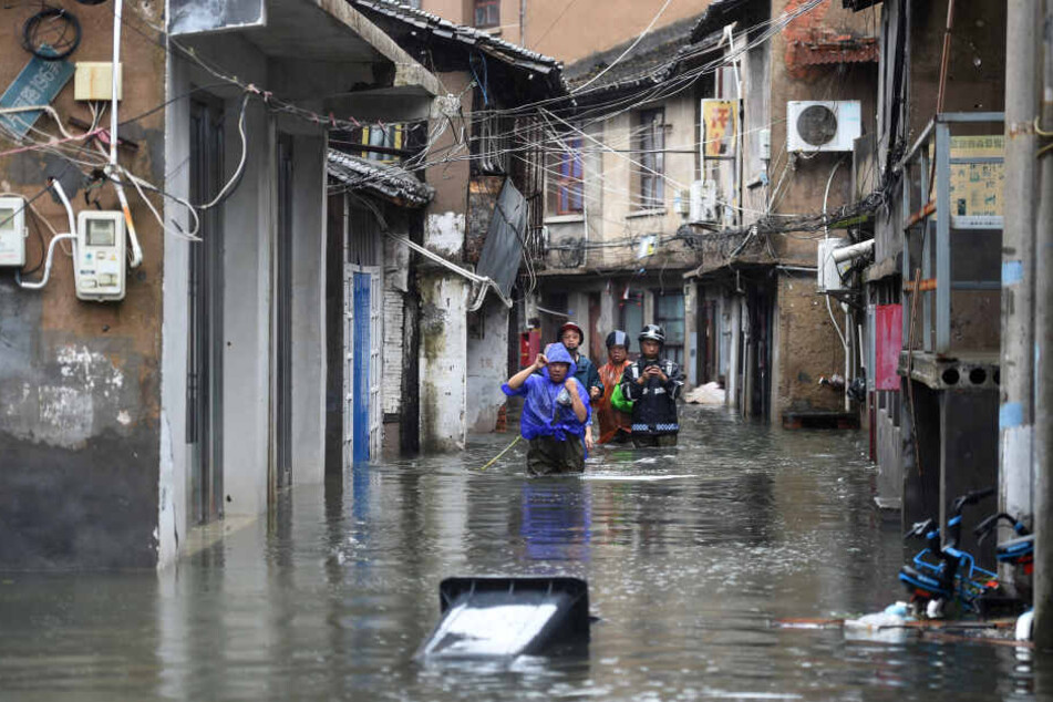 Menschen gehen zwischen Häusern auf einer von Wasser überfluteten Straße. Mit heftigem Regen und Sturmböen hat Taifun Lekima das chinesische Festland erreicht.