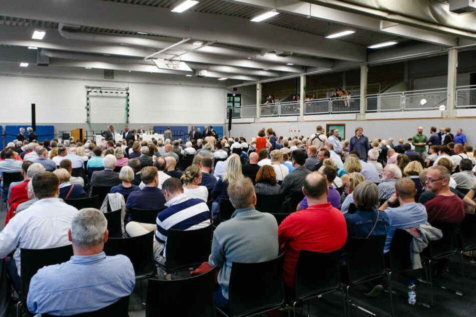 Einwohner der Gemeinde Boostedt sitzen während einer Bürgerversammlung in einer Sporthalle.