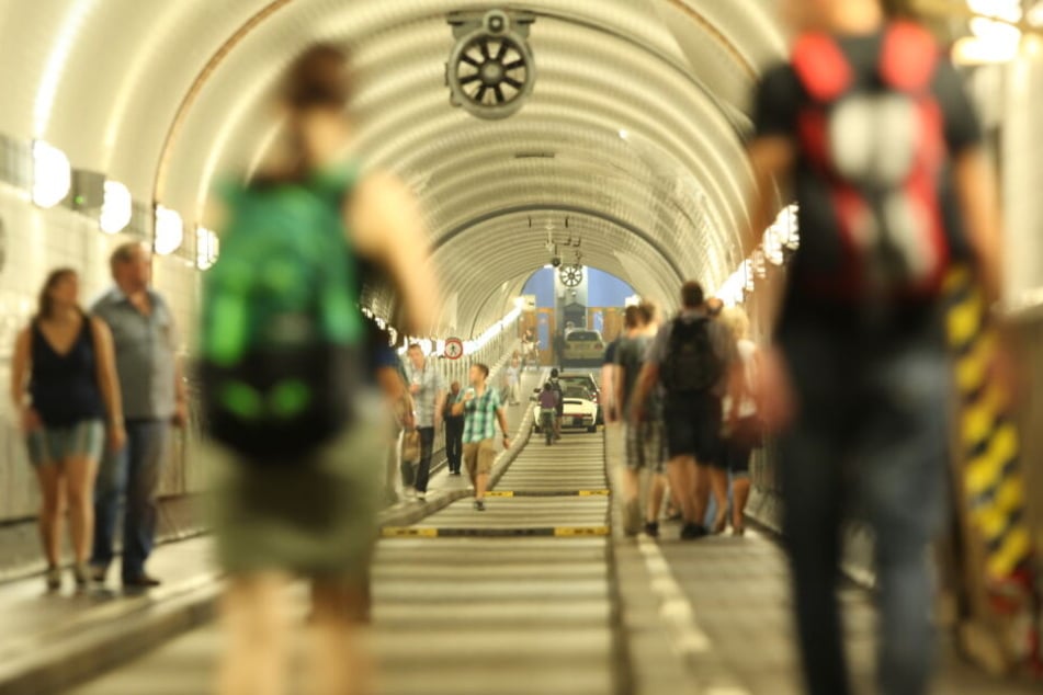 Passanten spazieren durch den Alten Elbtunnel in Hamburg, Fahrradfahrer und Autos cruisen ebenfalls entspannt durch die Röhre unter der Elbe.