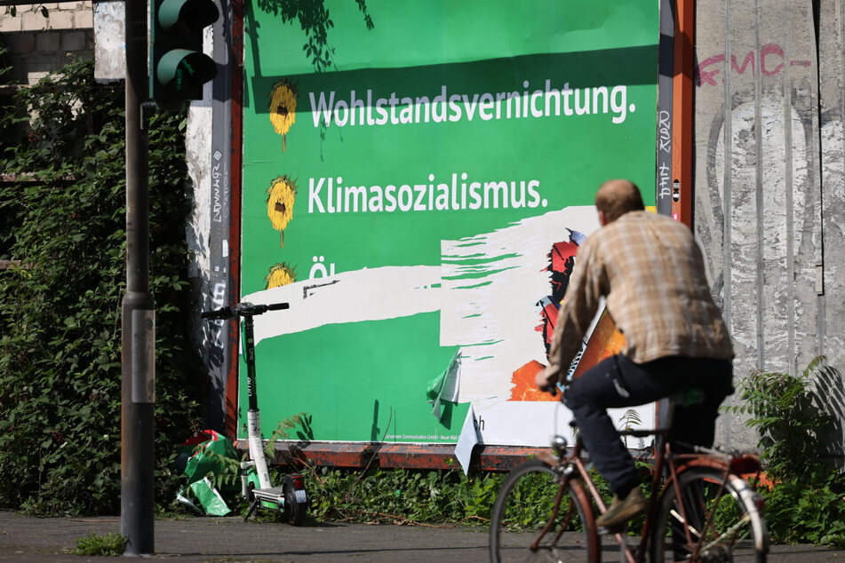 Ein beschädigtes Plakat mit den Schriftzügen "Wohlstandsvernichtung" und "Klimasozialismus" hängt an einem Straßenrand in Köln.