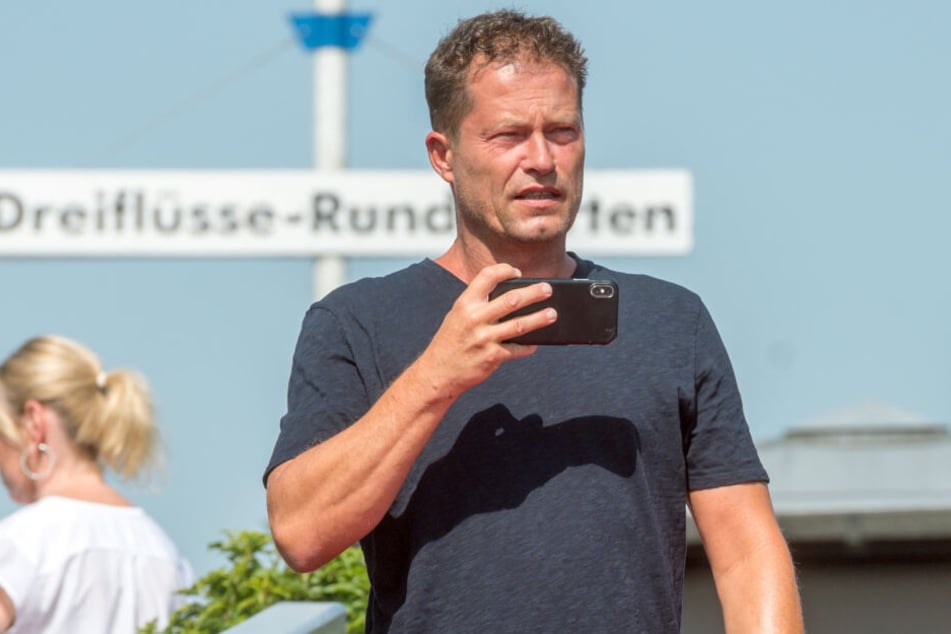Til Schweiger hält ein Smartphone in der Hand.