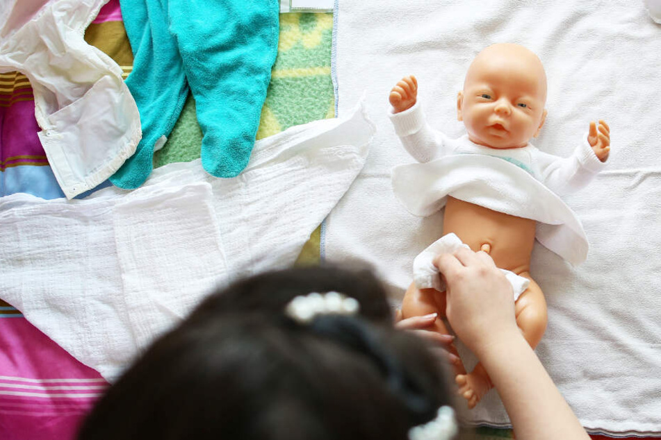 Eine Frau lernt in einer Schulung mit einer Puppe, wie Babys richtig gewickelt werden.