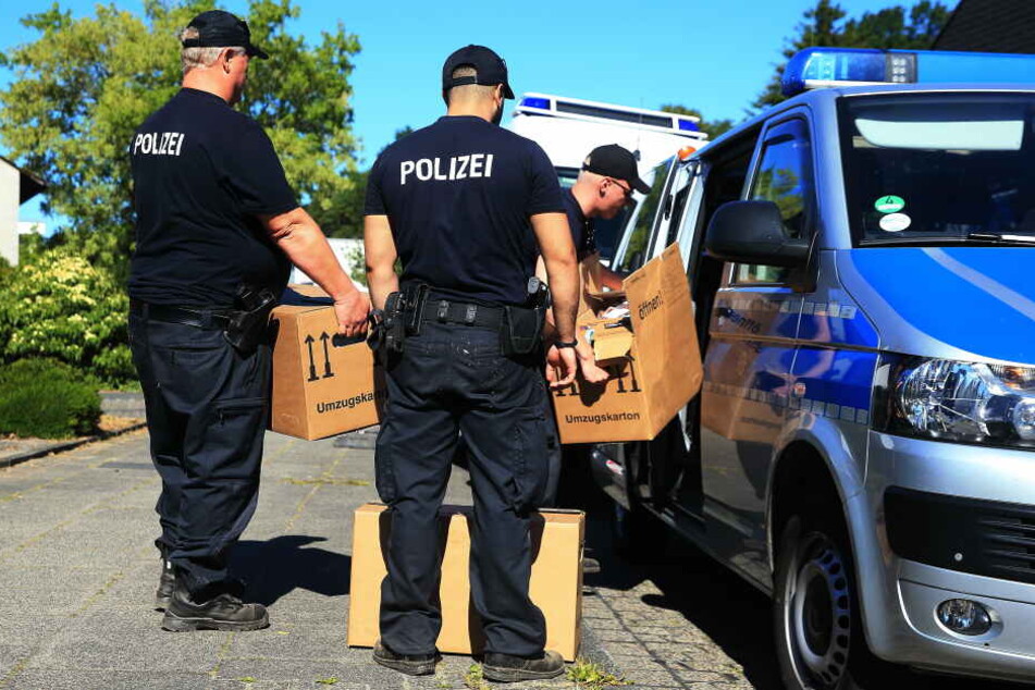 Polizisten tragen mehrere Kisten aus dem Haus des Tatverdächtigen und verstauen sie in einem Transporter.