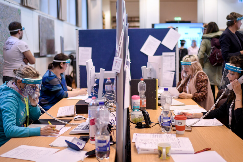 Mitarbeiter des Gesundheitsamtes Berlin-Mitte mit Gesichtsschutzschirm telefonieren im Lagezentrum des Gesundheitsamtes Mitte.