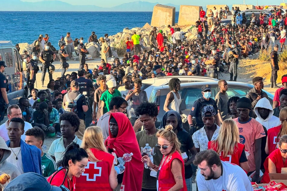 Migranten stehen Schlange, um Grundnahrungsmittel zu erhalten, die von Mitarbeitern des Roten Kreuzes verteilt werden.
