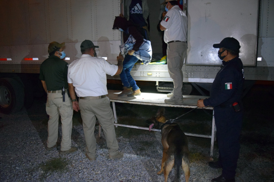 Mexikanische Polizisten und Offiziellle helfen den Migranten aus den Sattelzügen heraus.