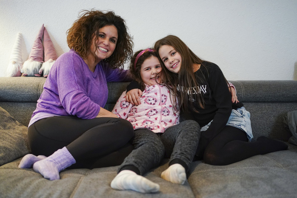 Daniela Bilke (l.) und ihre beiden Töchter Enna (6, M.) und Luisa sitzen in ihrem Wohnzimmer auf dem Sofa.