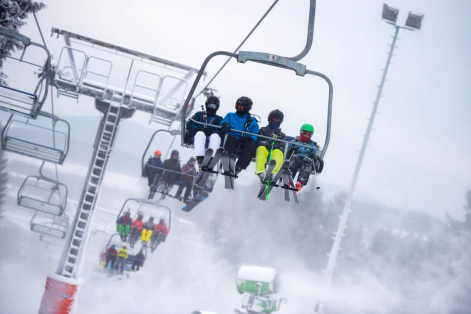 Skifahrer sitzen auf einem Sessellift im Skigebiet Winterberg und fahren durch den Kunstschnee der Schneekanonen (Archivbild).