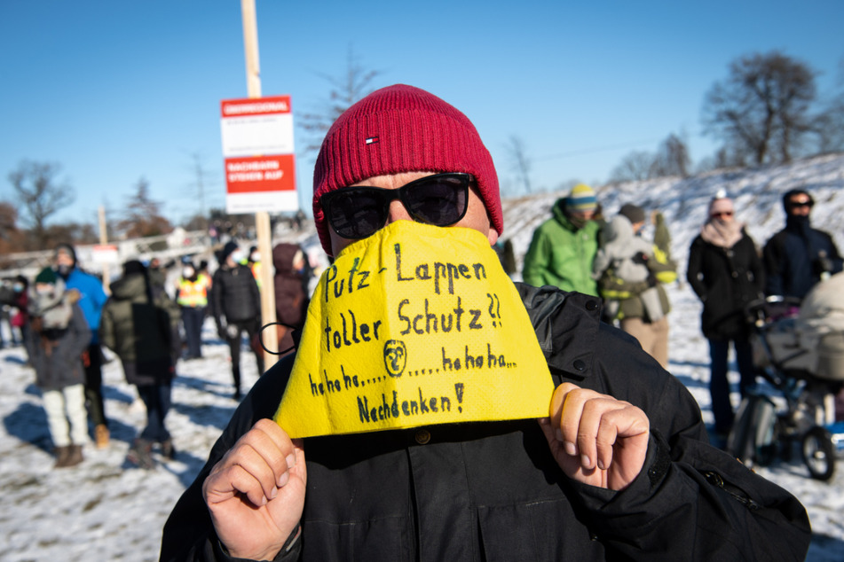Ein Demonstrationsteilnehmer trägt einen Lappen mit der Aufschrift "Putz-Lappen toller Schutz?? hahaha - hahaha - Nachdenken!" als Mundschutz.