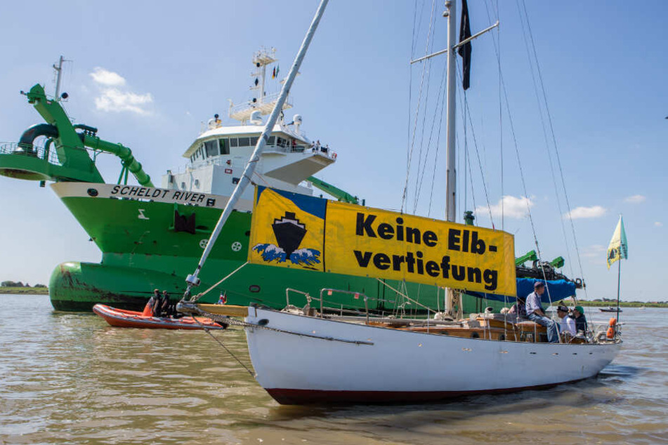 Gegner der Elbvertiefung begleiten das Baggerschiff mit Booten und Bannern auf der Elbe.