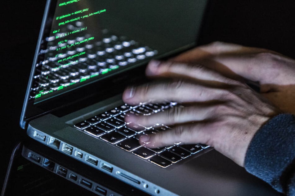Ein Mann tippt auf einer beleuchteten Tastatur eines Laptops, während auf dem Monitor ein Hacker-Programm geöffnet ist.