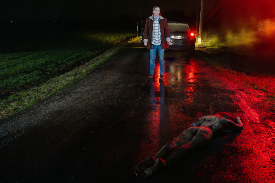 XY-Szenenfoto: Eine Autofahrerin findet eine nackte Tote auf der Straße.