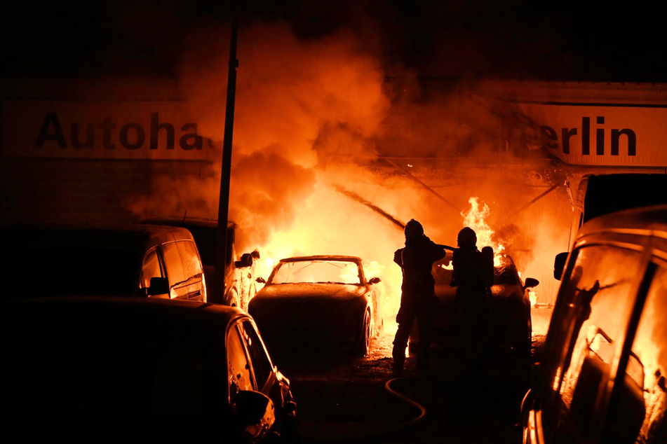 Lodernde Flammen griffen von brennenden Autos auf ein Gebäude über.