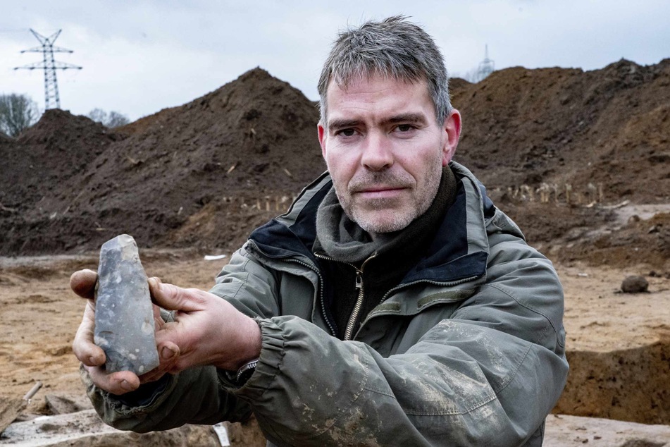 Ringo Klooß, Grabungsleiter, zeigt in der Ausgrabungsstelle eines Großsteingrabes aus der Trichterbecherzeit ein darin gefundenes Feuersteinbeil.