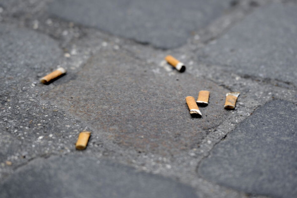 Zigarettenkippen liegen auf einem Gehweg mit Pflastersteinen