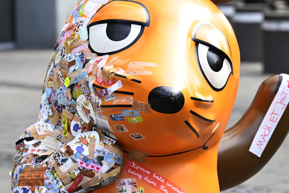 Passanten beklebten die lädierte Maus-Figur in Köln mit etlichen bunten Pflastern.