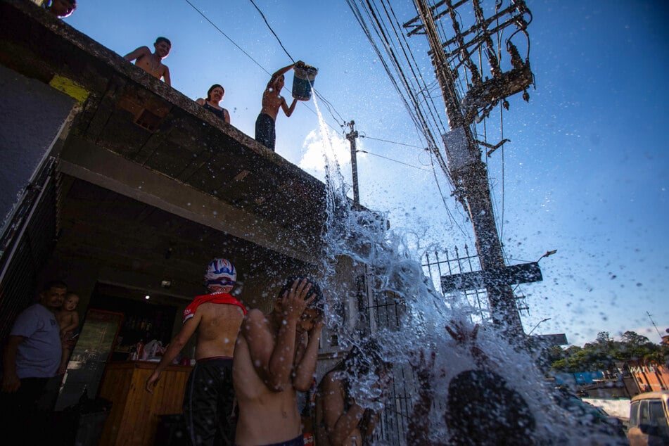 Kinder gießen Wasser aus einem Eimer von einem Dach in São Paulo.
