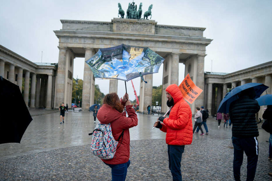 Eine Passantin kämpft mit ihrem Regenschirm vor dem Brandenburger Tor gegen den Wind.