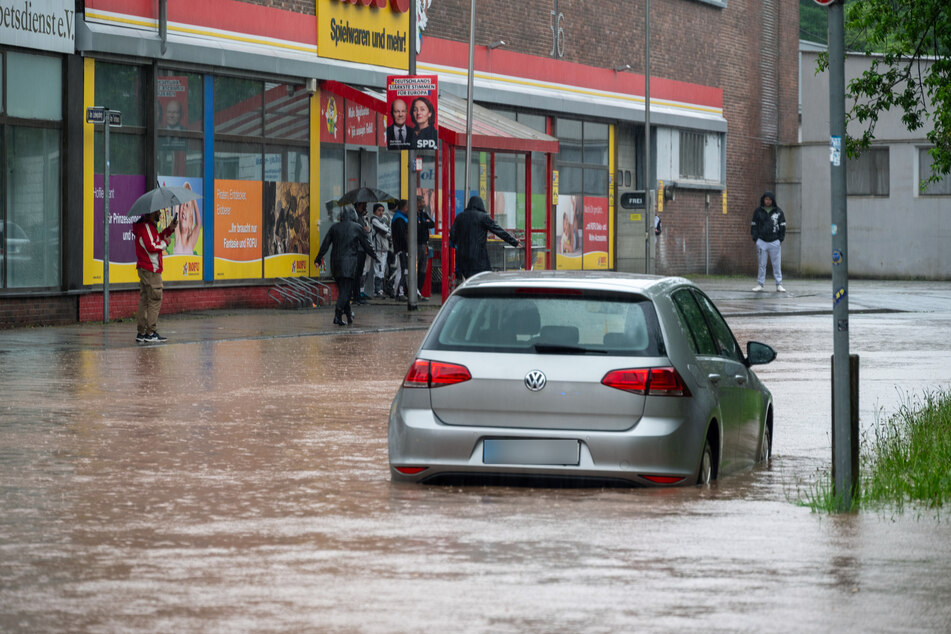 Passanten stapfen und fahren durch das Hochwasser in der Fischbachstrasse in Saarbrücken. Nach starken Regenfällen steht diese teilweise unter Wasser.